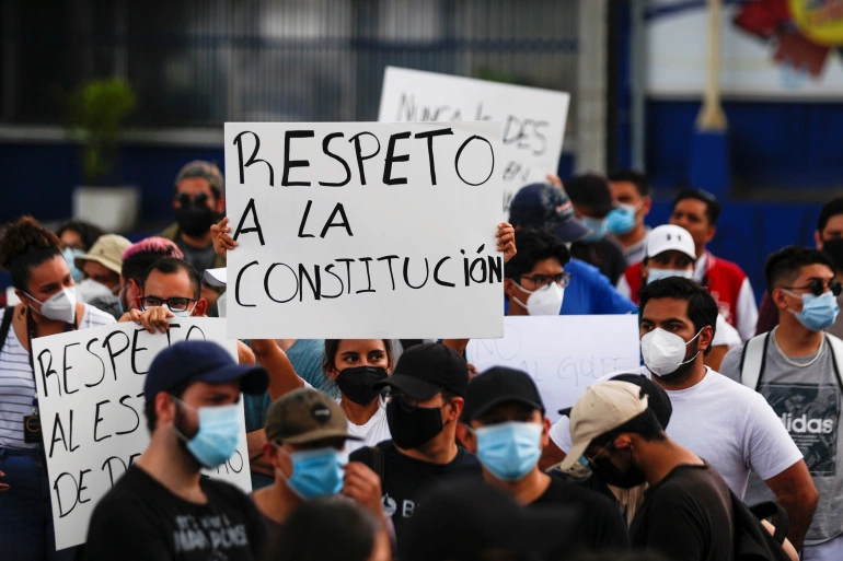 People hold signs reading "Respect the constitution," in protest against the removal of Supreme Court judges and the Attorney General by El Salvador's congress, in San Salvador, 2 May 2021 (photo credit: Jose Cabezas / Reuters).
