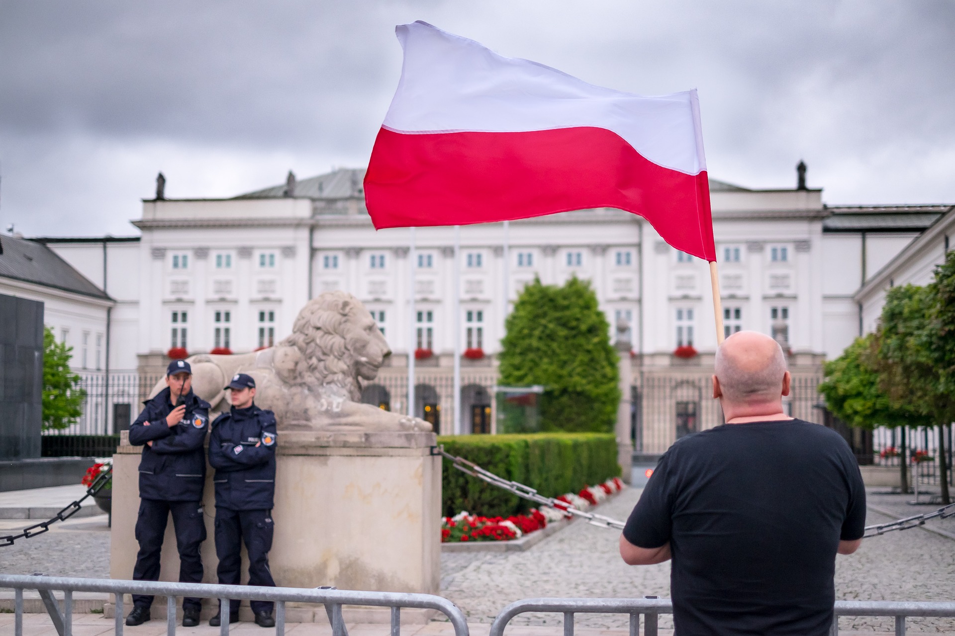 A man holding a Polish flag in front of the presidential palace in Warsaw (Photo credit: Pixabay)